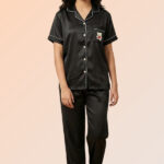 Woman wearing a black cotton brush front-open pajama top with a teddy bear pocket and matching long pants.