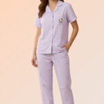 Woman smiling in a lavender 2-piece sleepwear set featuring a cotton brush button-down shirt with a character pocket and long pajama bottoms.