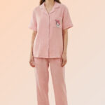 Woman modeling a pretty pink 2-piece nightwear set made of cotton brush, featuring a character pocket shirt and long pajama bottoms.