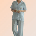 Woman holding a mug wearing a light blue cotton brush pajama set, consisting of a front-open shirt with a bear patch and long pants.