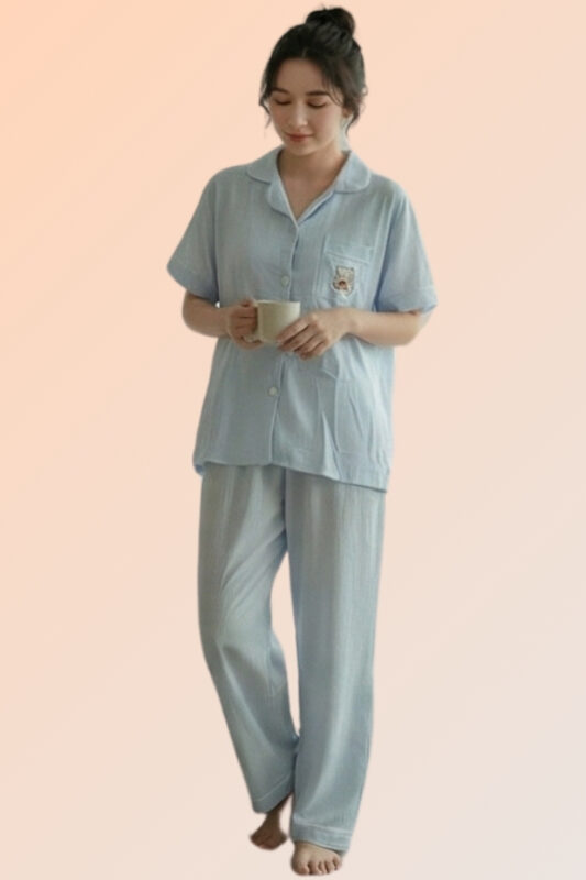 Woman holding a mug wearing a light blue cotton brush pajama set, consisting of a front-open shirt with a bear patch and long pants.