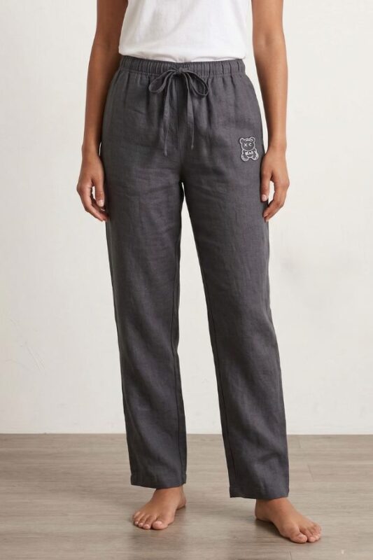 A front shot of a barefoot woman standing against a plain background, modeling charcoal gray wide-leg linen pajama pants paired with a white t-shirt.