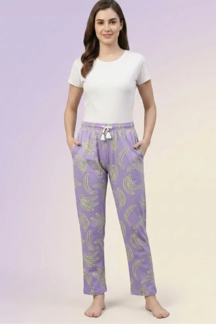 Full-body shot of a model wearing light purple banana print women's pajamas with neon outlines, drawstring with tassels, and hands in pockets.