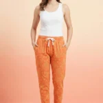 Full-body shot of a model wearing cheerful orange popcorn print women's pajamas with yellow popcorn buckets, white drawstring with tassels, and grey slippers.