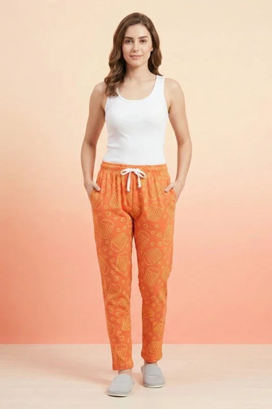 Full-body shot of a model wearing cheerful orange popcorn print women's pajamas with yellow popcorn buckets, white drawstring with tassels, and grey slippers.