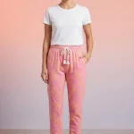 Full-body image of a model wearing sweet pink pretzel print women's pajamas with yellow pretzels, white drawstring with tassels, and bare feet.
