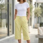 Smiling woman posing in a pastel yellow cotton capri and white top outdoors.