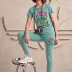 Woman wearing a mint green cotton t-shirt and pajama pants set with an urban bear graphic that says 'Street Rules', standing next to a metal stool.