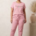 Woman modeling a pink cotton relaxed fit pajama set with heart graphics and the text Live in the moment.