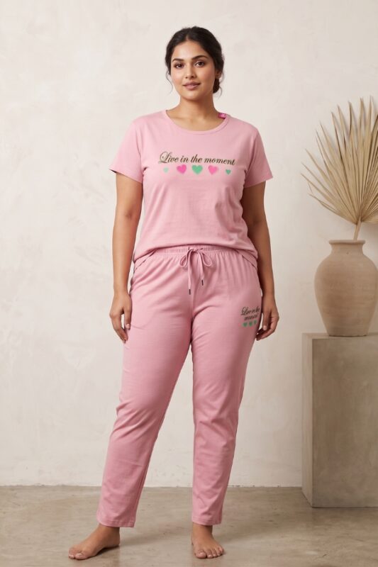 Woman modeling a pink cotton relaxed fit pajama set with heart graphics and the text Live in the moment.