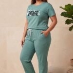 Woman wearing a sage green relaxed fit cotton pajama set with the word Peace and daisy graphics printed on the shirt.